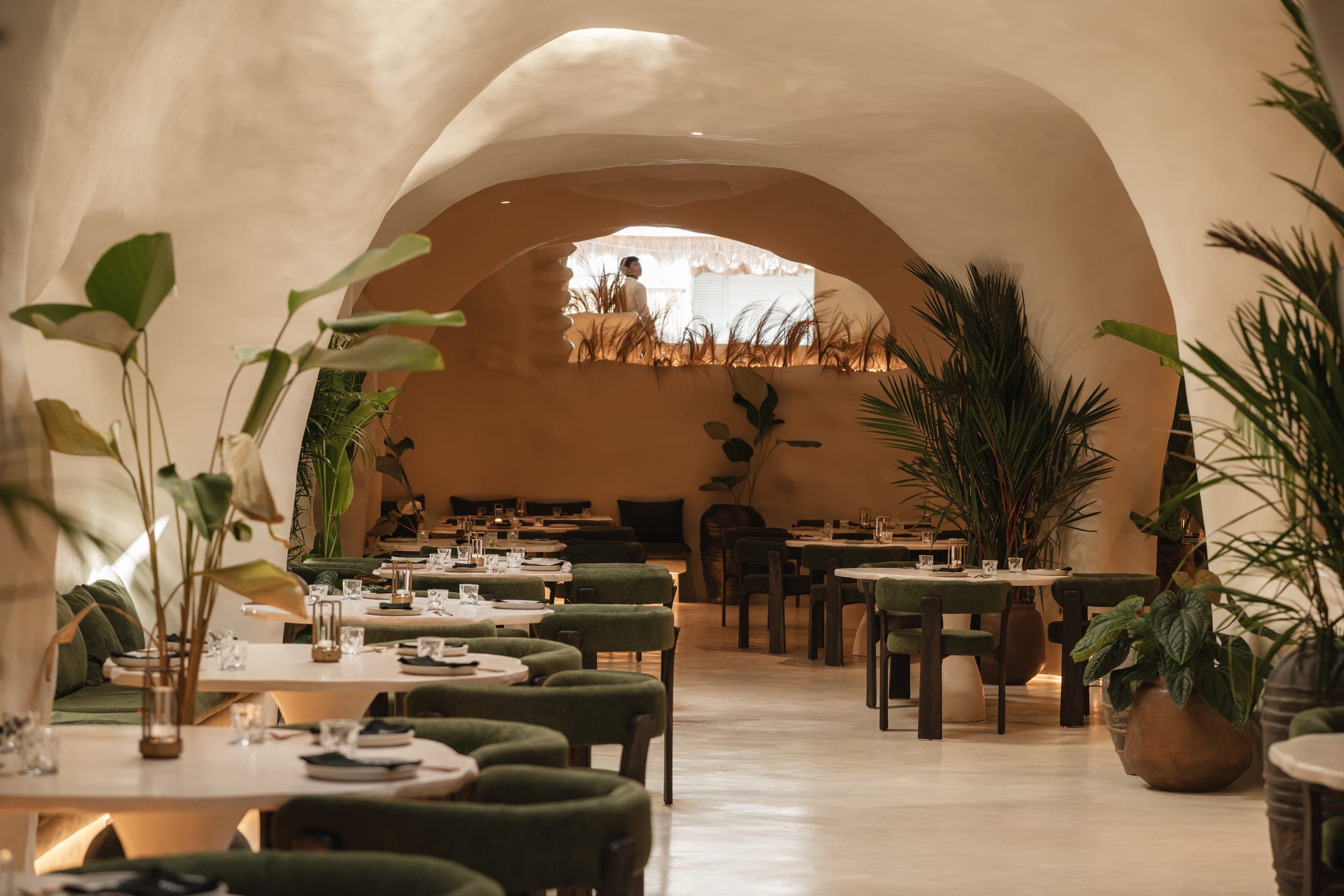 The KAJA dining room: hand-sculpted plaster arches, olive velvet chairs and palms under warm light